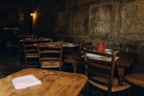 A sala antes do serviço: mesas de madeira, cadeiras de tabua e parede de granito